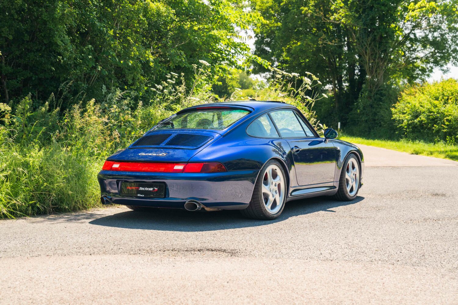 blue porsche parked next to a green forest